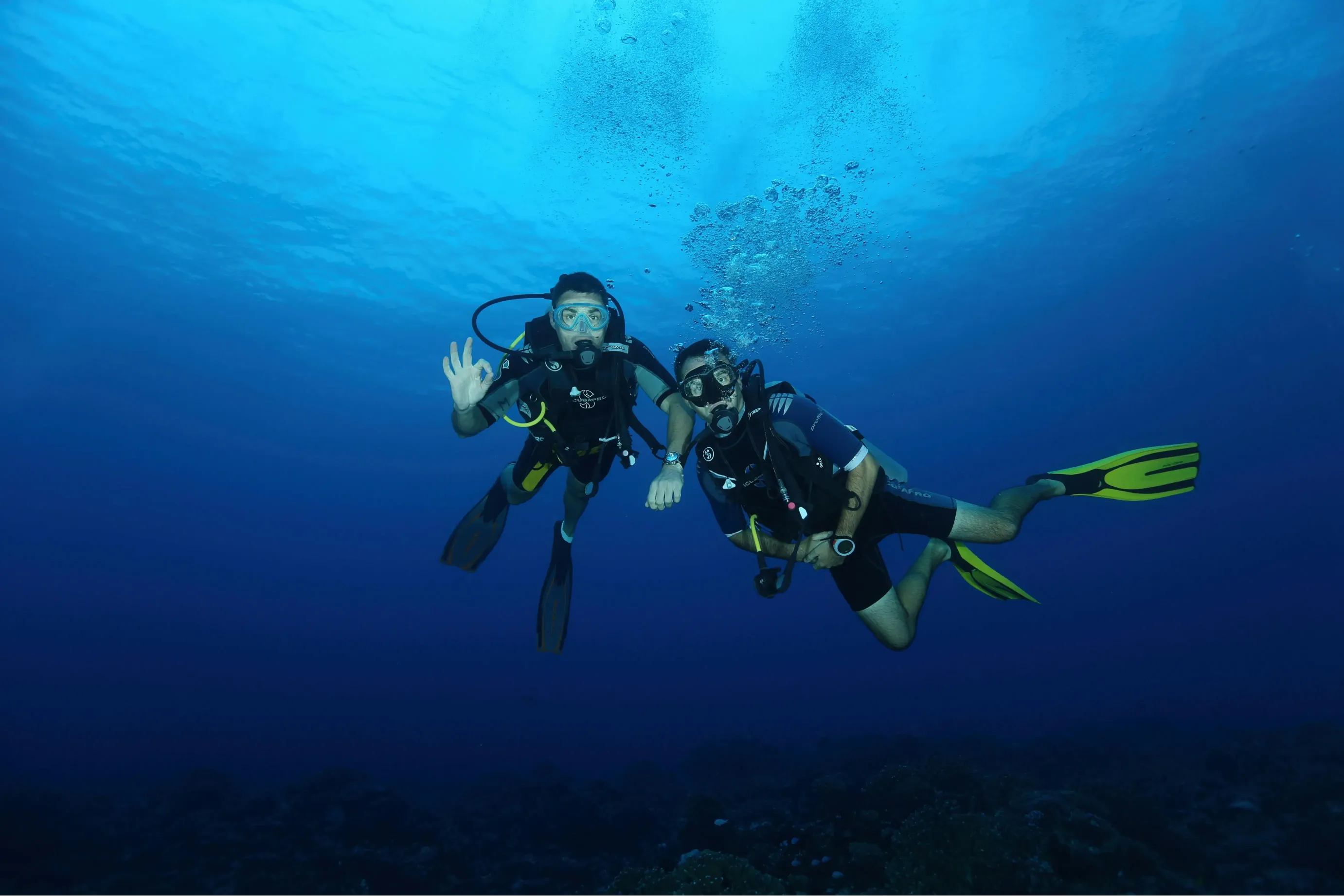 Two scuba divers swimming underwater and signalling to each other during a dive.