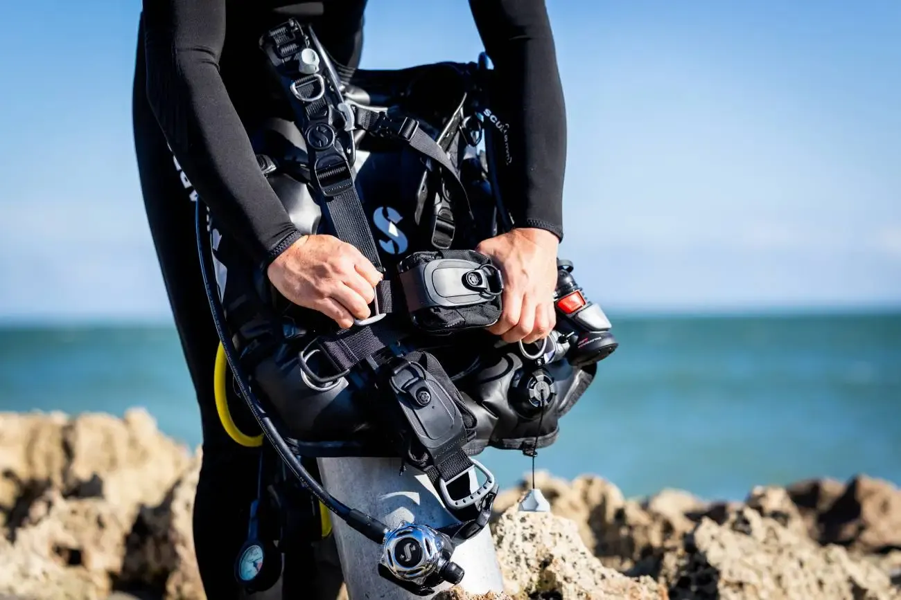Scuba diver holding an underwater camera housing while standing beside the sea.